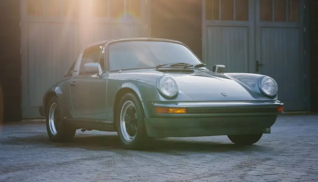 Porsche 911 SC 3.0 Targa Baujahr 1983 in Schieferblau metallic im Hof vor Garagen, Sonnenstrahlen fallen auf das Auto