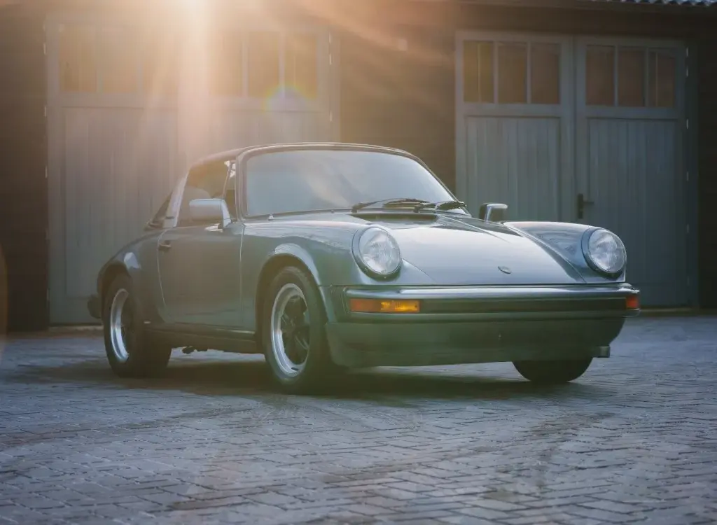 Porsche 911 SC 3.0 Targa Baujahr 1983 in Schieferblau metallic im Hof vor Garagen, Sonnenstrahlen fallen auf das Auto