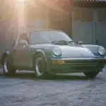Porsche 911 SC 3.0 Targa Baujahr 1983 in Schieferblau metallic im Hof vor Garagen, Sonnenstrahlen fallen auf das Auto
