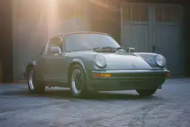 Porsche 911 SC 3.0 Targa Baujahr 1983 in Schieferblau metallic im Hof vor Garagen, Sonnenstrahlen fallen auf das Auto