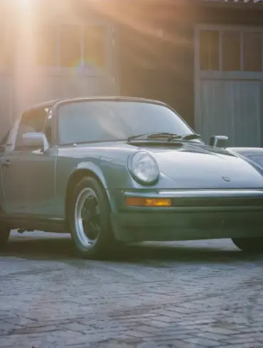 Porsche 911 SC 3.0 Targa Baujahr 1983 in Schieferblau metallic im Hof vor Garagen, Sonnenstrahlen fallen auf das Auto