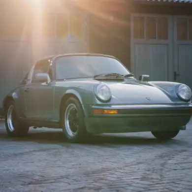 Porsche 911 SC 3.0 Targa Baujahr 1983 in Schieferblau metallic im Hof vor Garagen, Sonnenstrahlen fallen auf das Auto