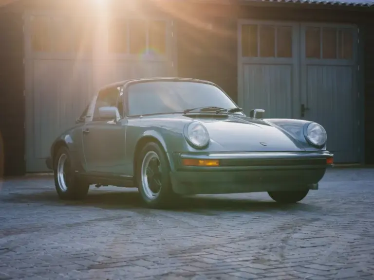 Porsche 911 SC 3.0 Targa Baujahr 1983 in Schieferblau metallic im Hof vor Garagen, Sonnenstrahlen fallen auf das Auto
