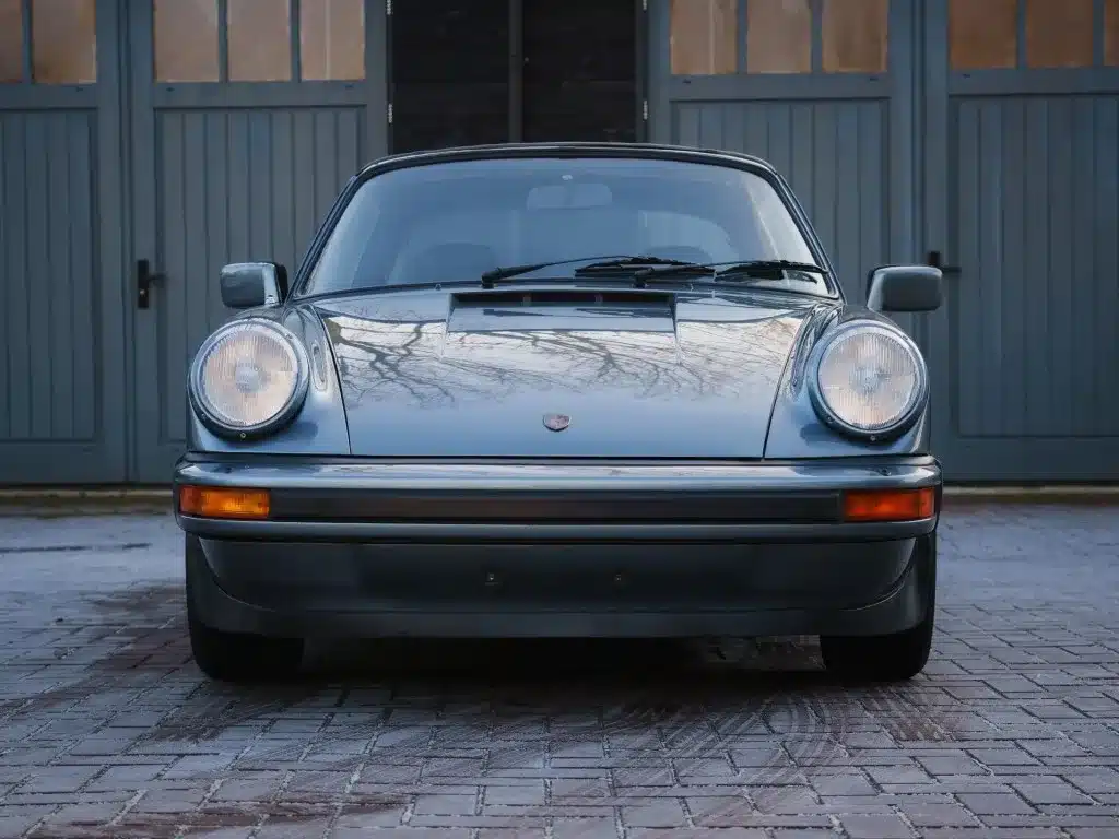 Frontansicht eines Porsche 911 SC 3.0 Targa aus dem Jahr 1983 in Schieferblau metallic vor Garagentoren.