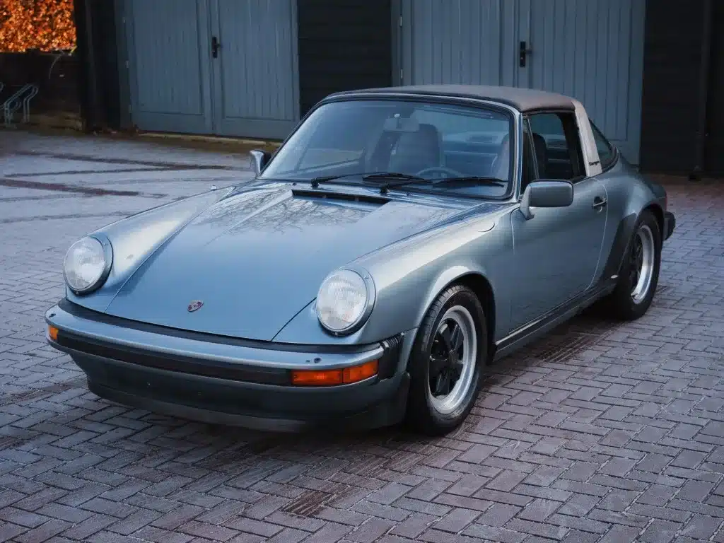 Porsche 911 SC 3.0 Targa von 1983 in Schieferblau metallic, frontal und seitlich aufgenommen, geparkt auf Pflastersteinen.