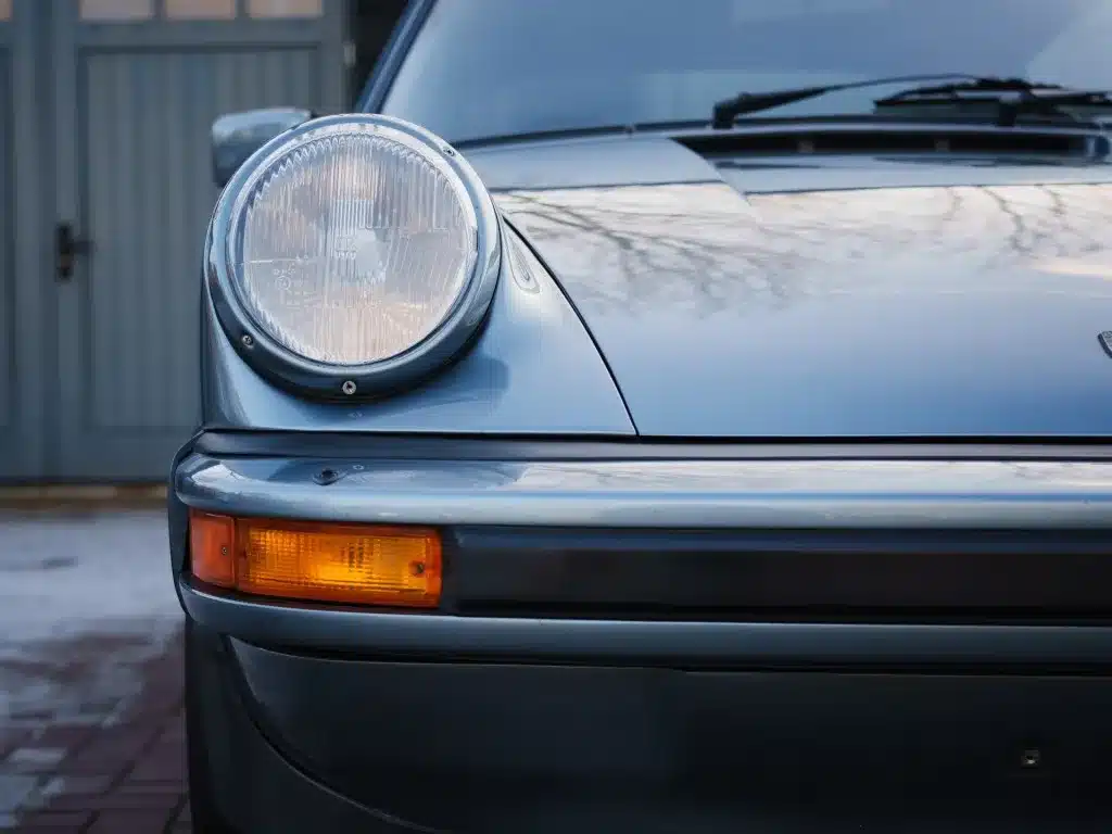 Nahaufnahme der linken Front eines Porsche 911 SC 3.0 Targa in Schieferblau metallic mit Scheinwerfer und Blinker
