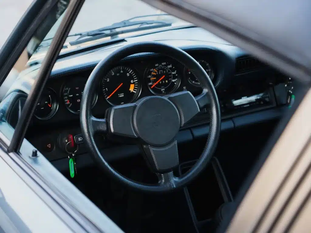 Innenraum und Lenkrad eines Porsche 911 SC 3.0 Targa, Baujahr 1983, mit schwarzem Armaturenbrett und Rundinstrumenten.