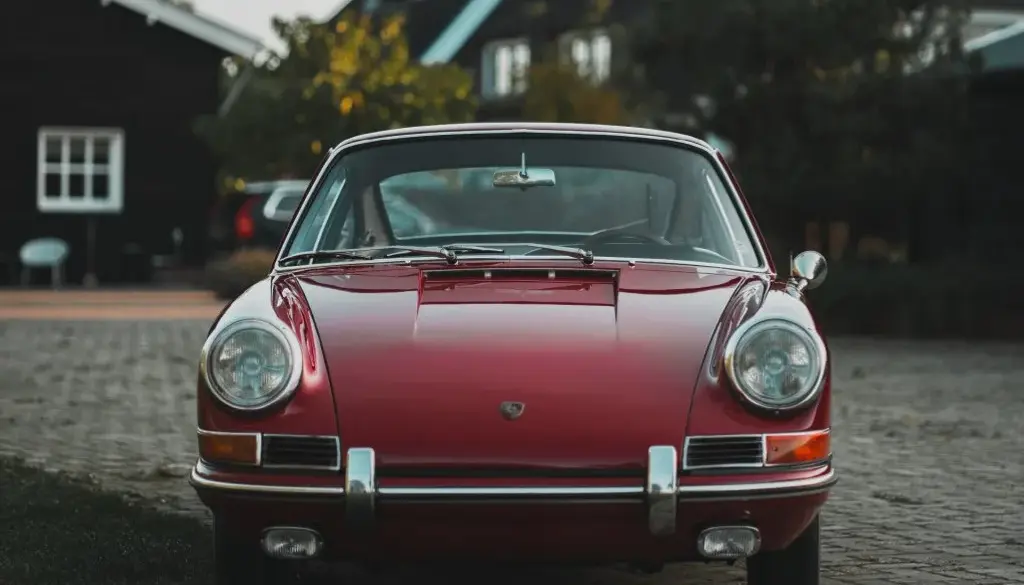 Frontale Ansicht eines rubinroten Porsche 911 Coupé Baujahr 1965, klassisches Design mit runden Scheinwerfern und Chromstoßstange.
