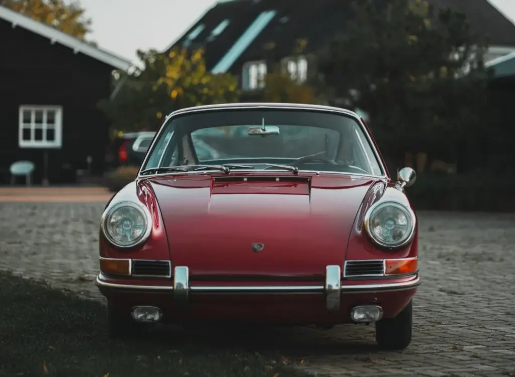 Frontale Ansicht eines rubinroten Porsche 911 Coupé Baujahr 1965, klassisches Design mit runden Scheinwerfern und Chromstoßstange.