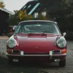 Frontale Ansicht eines rubinroten Porsche 911 Coupé Baujahr 1965, klassisches Design mit runden Scheinwerfern und Chromstoßstange.