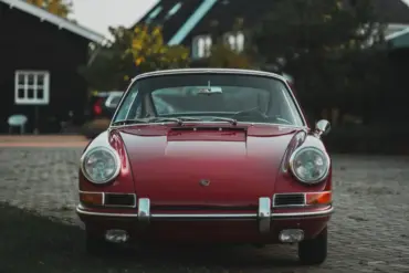 Frontale Ansicht eines rubinroten Porsche 911 Coupé Baujahr 1965, klassisches Design mit runden Scheinwerfern und Chromstoßstange.