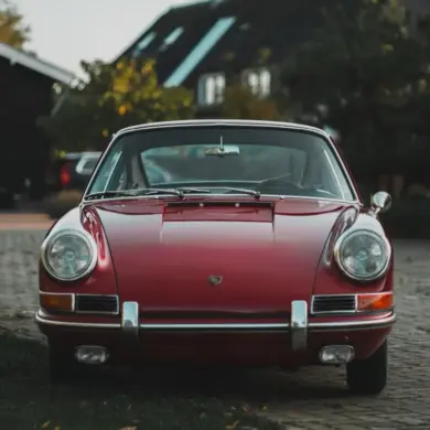 Frontale Ansicht eines rubinroten Porsche 911 Coupé Baujahr 1965, klassisches Design mit runden Scheinwerfern und Chromstoßstange.