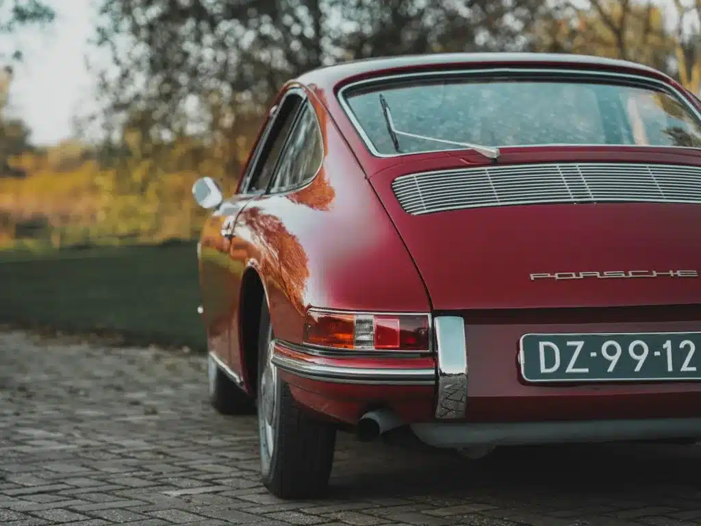 Rückansicht eines Porsche 911 von 1965 in rubinroter Farbe, geparkt auf einem Steinpflasterweg mit sichtbarem Kennzeichen