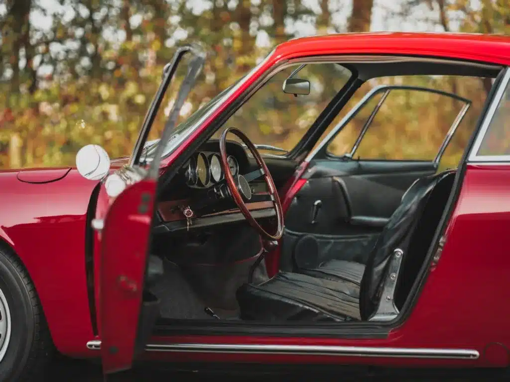 Offene Fahrertür eines Porsche 911 von 1965, rubinrote Lackierung, Blick auf das originale schwarze Interieur und das typisch gestaltete Armaturenbrett.