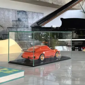 Skulptur eines klassischen Porsche 934 aus lackiertem Buchenholz in einer Glasvitrine auf einem Tisch, mit modernem Interieur im Hintergrund.