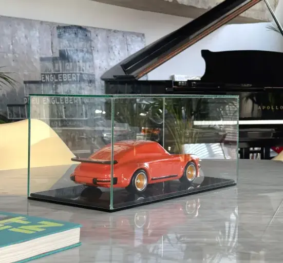 Skulptur eines klassischen Porsche 934 aus lackiertem Buchenholz in einer Glasvitrine auf einem Tisch, mit modernem Interieur im Hintergrund.