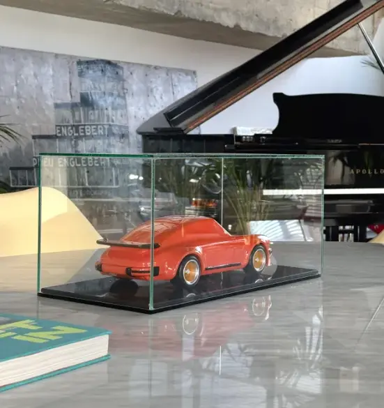 Skulptur eines klassischen Porsche 934 aus lackiertem Buchenholz in einer Glasvitrine auf einem Tisch, mit modernem Interieur im Hintergrund.