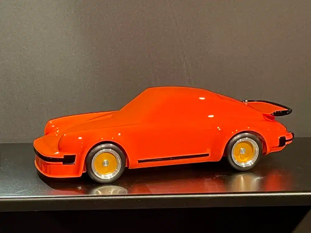 Rote Autoskulptur „80 Turbo Gr4“ aus massivem Buchenholz, Design angelehnt an den Porsche 934, auf schwarzem Untergrund.