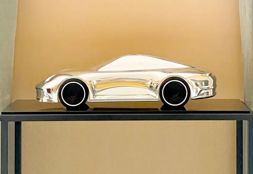Aluminium-Skulptur eines Porsche 992 auf schwarzem Sockel mit hochglanzpolierter Oberfläche und schwarzen Felgen.