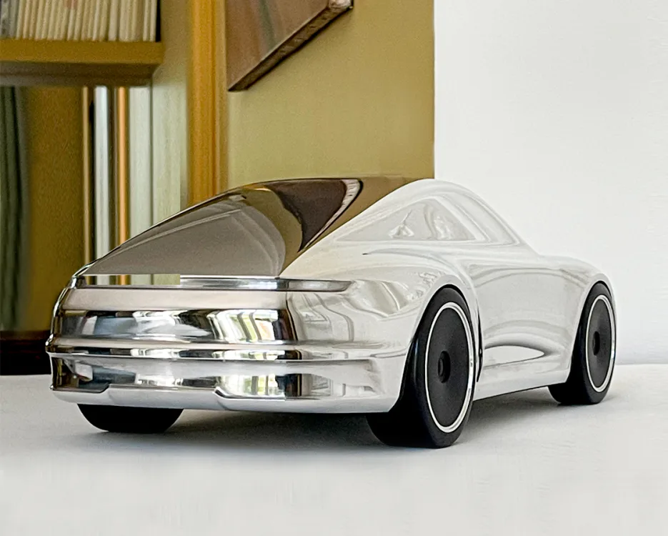 Abstrakte Aluminium-Skulptur des Porsche 911 (992) als Designobjekt mit polierter Oberfläche und schwarzen Felgen.