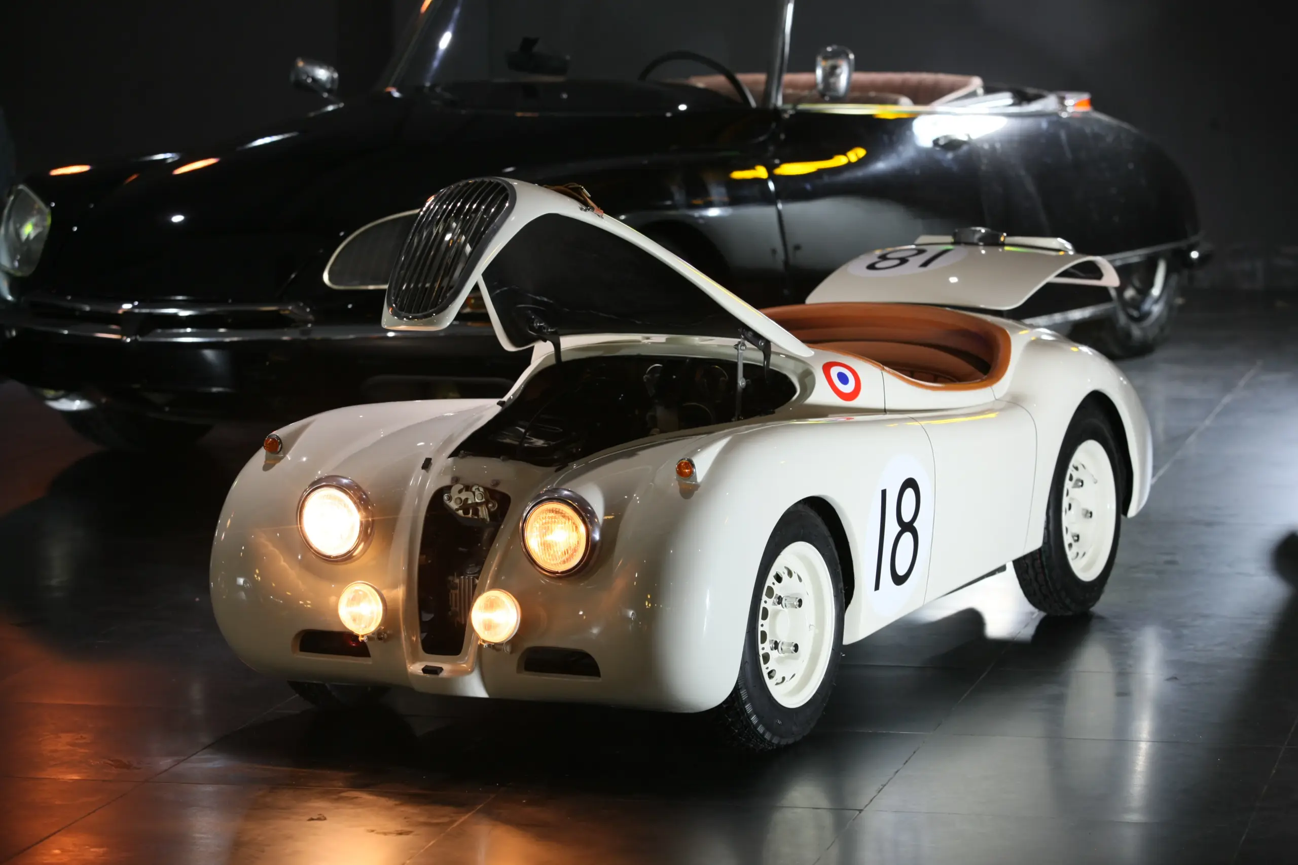 Verkleinerte Replik eines Jaguar XK120 Roadsters in Weiß mit geöffnetem Motorraum und eingeschaltetem Scheinwerferlicht