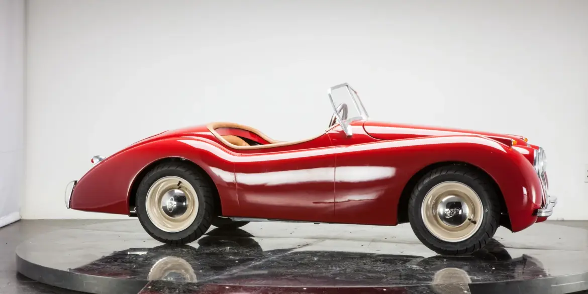 Seitliche Ansicht eines XK120 Roadster Red als verkleinerte Replik, handgefertigt mit roter Karosserie, Aluminiumelementen und klassischen Details.
