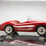 Seitliche Ansicht eines XK120 Roadster Red als verkleinerte Replik, handgefertigt mit roter Karosserie, Aluminiumelementen und klassischen Details.