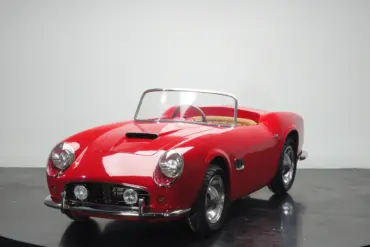 Rotes Spyder Junior Car im Stil eines klassischen Sportwagens, halbgroßes Kinderfahrzeug auf schwarzem Studiohintergrund.