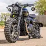 Thornton Hundred Adventure Bobber mit grobstolligen Reifen, breiten Speichenrädern und individueller Ausstattung auf einem asphaltierten Platz.