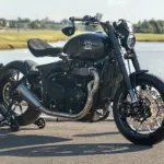 Thornton Hundred EVO Bobber Motorrad mit Carbon-Rädern, sportlichem Design und reduzierter Bobber-Optik seitlich am Straßenrand vor einem Gewässer.