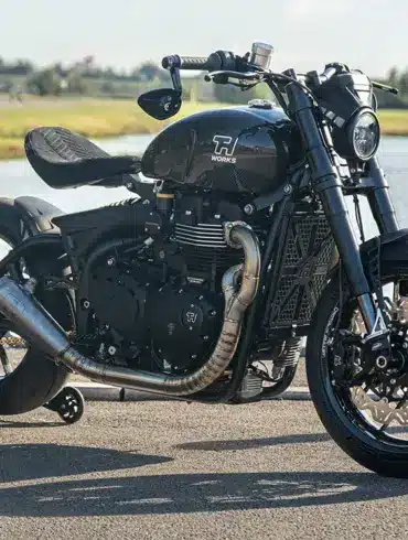 Thornton Hundred EVO Bobber Motorrad mit Carbon-Rädern, sportlichem Design und reduzierter Bobber-Optik seitlich am Straßenrand vor einem Gewässer.