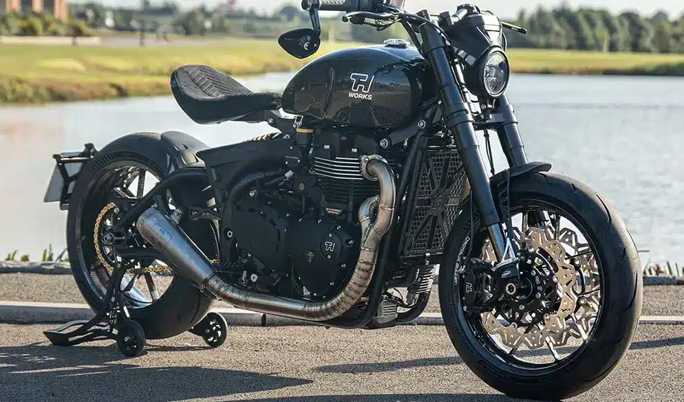 Thornton Hundred EVO Bobber Motorrad mit Carbon-Rädern, sportlichem Design und reduzierter Bobber-Optik seitlich am Straßenrand vor einem Gewässer.