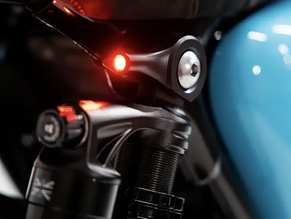 Detailansicht eines LED-Blinkers und eines Federbeins an einer Thornton Hundred Triumph T120, mit sichtbarem blauen Tank