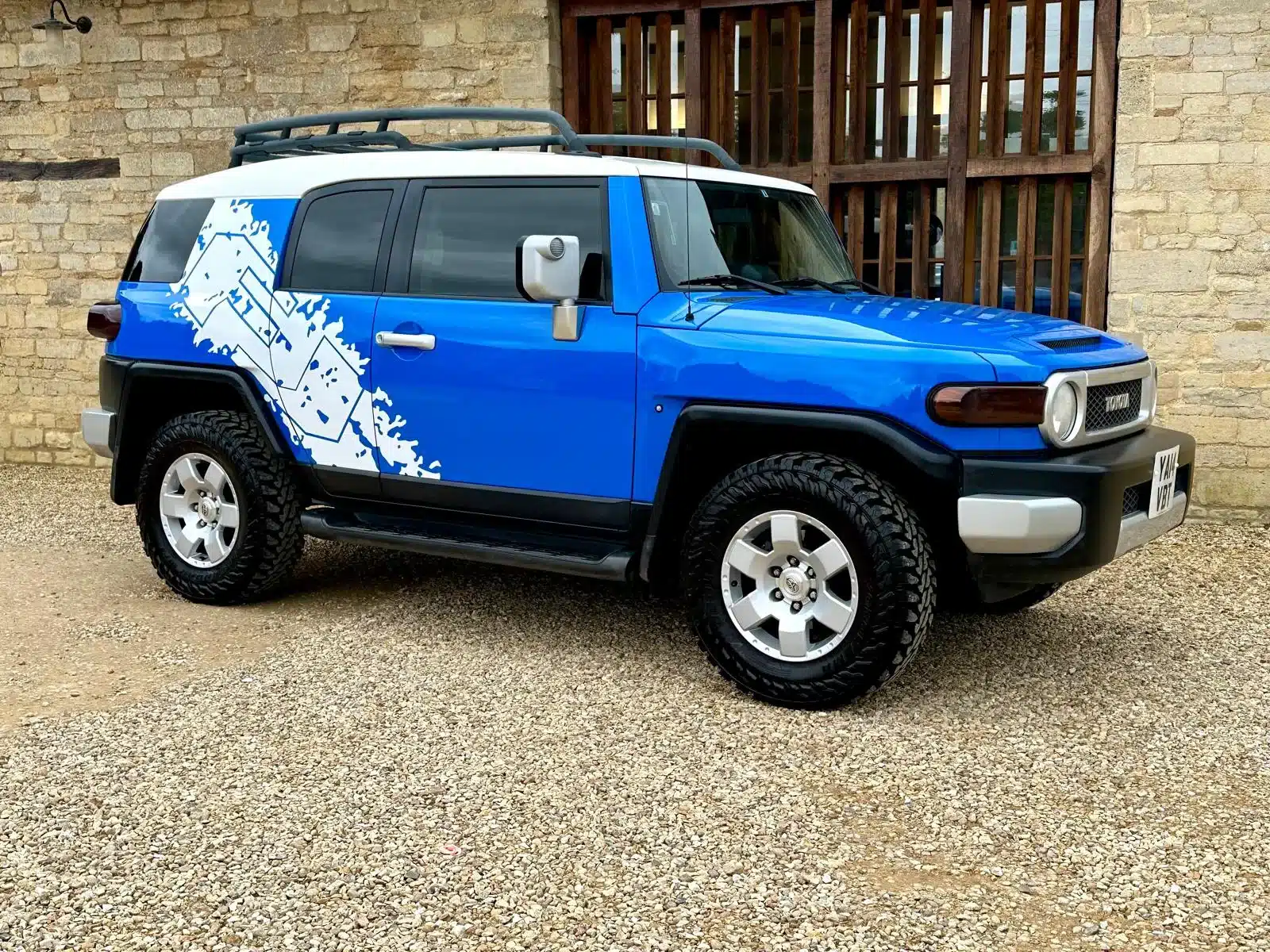 Toyota FJ Cruiser 4.0 V6, Bali-Blau mit weißem Dach, Expeditions-Dachträger und Yokohama-Mud-Terrain-Reifen seitlich aufgenommen