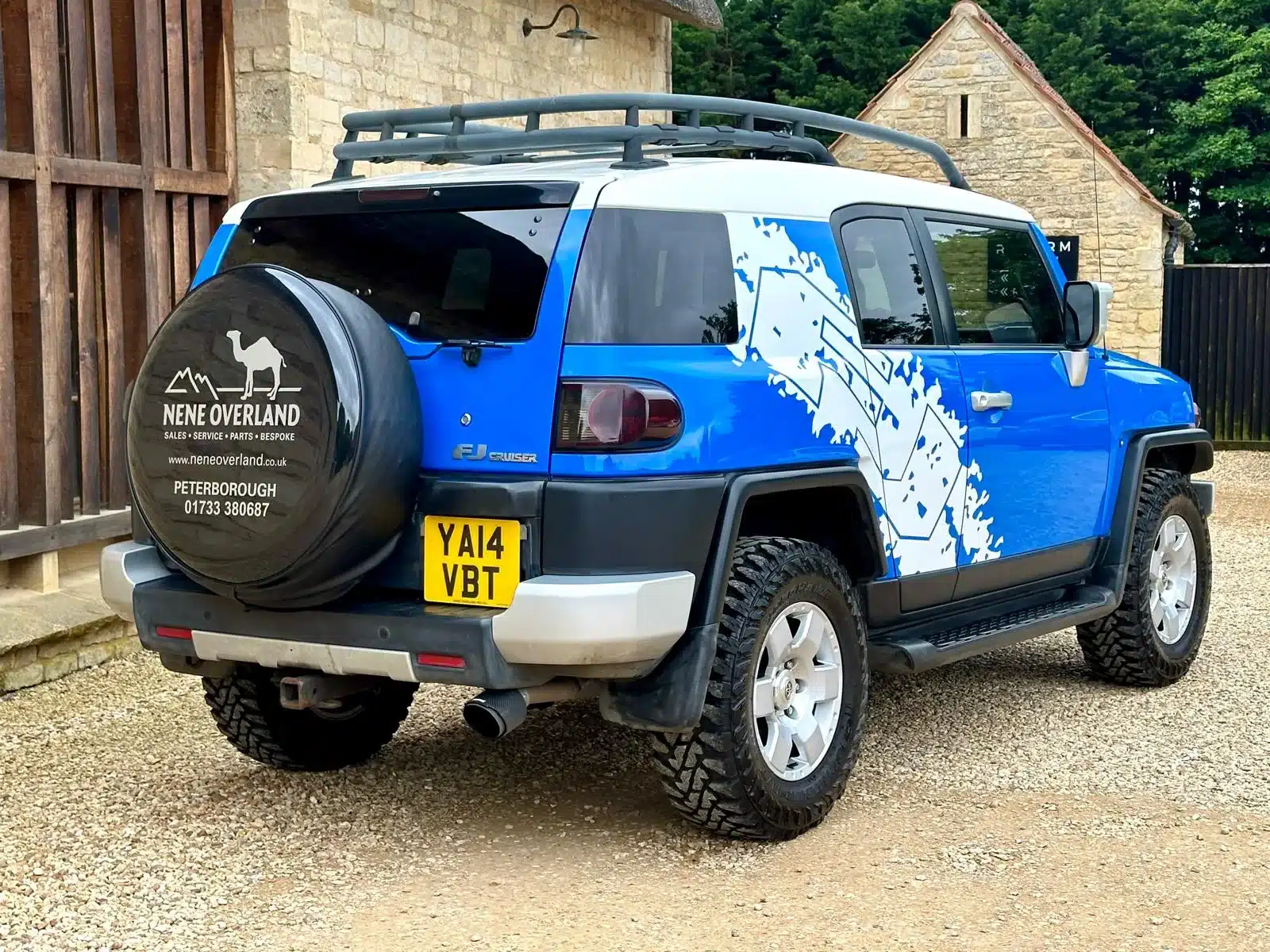 Heck- und Seitenansicht eines blauen Toyota FJ Cruiser mit weißem Dach, Dachträger und Expeditionsausstattung.