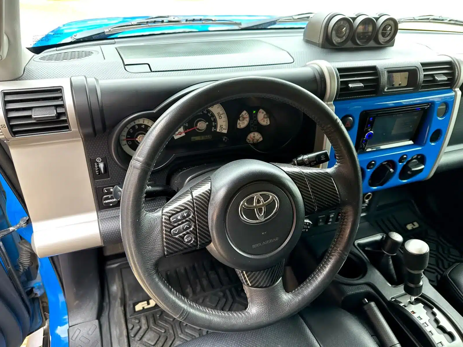 Innenraumansicht eines Toyota FJ Cruiser 4.0 V6 mit Lenkrad, Automatikschaltung und blauen Designelementen.