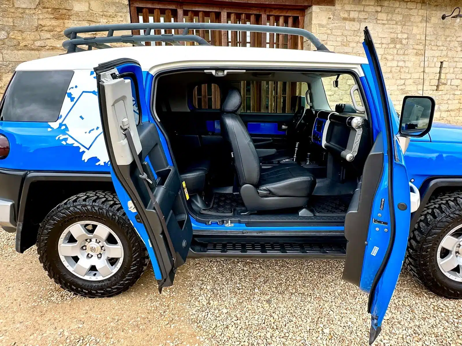 Toyota FJ Cruiser 4.0 V6 in Bali-Blau mit weißen Dach und geöffneter Halbtür, Seitenansicht des Innenraums und der markanten Offroad-Bereifung.