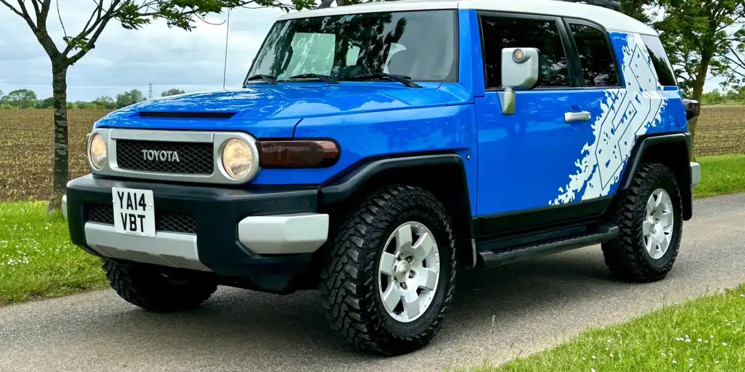 Toyota FJ Cruiser 4.0 V6 in Bali-Blau mit weißem Dach, Expeditions-Dachträger und Yokohama-Mud-Terrain-Reifen auf einer Straße.