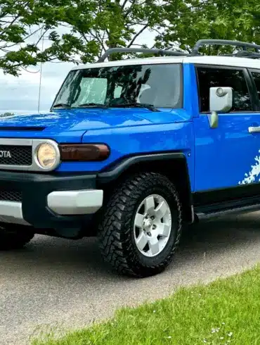 Toyota FJ Cruiser 4.0 V6 in Bali-Blau mit weißem Dach, Expeditions-Dachträger und Yokohama-Mud-Terrain-Reifen auf einer Straße.