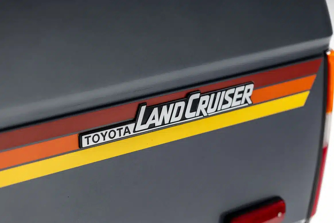 Heckemblem eines Toyota Land Cruiser FJ62 mit Farbstreifen in Rot, Orange und Gelb.