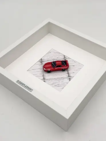 Gerahmtes Modell eines roten Toyota Supra Mk IV im Maßstab 1:64 in einem weißen Kastenrahmen von oben fotografiert