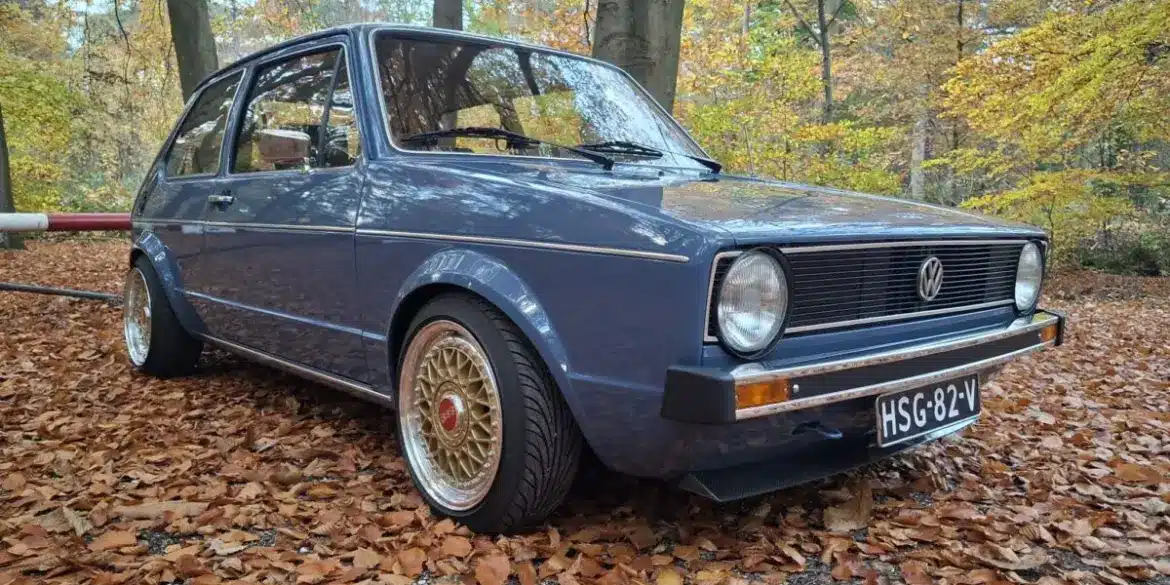 Restaurierter VW Golf I von 1981 mit blauer Lackierung und BBS-Felgen, geparkt auf Laub im Wald, seitliche Frontansicht.