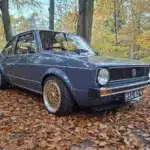 Restaurierter VW Golf I von 1981 mit blauer Lackierung und BBS-Felgen, geparkt auf Laub im Wald, seitliche Frontansicht.