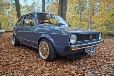Restaurierter VW Golf I von 1981 mit blauer Lackierung und BBS-Felgen, geparkt auf Laub im Wald, seitliche Frontansicht.