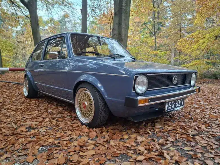 Restaurierter VW Golf I von 1981 mit blauer Lackierung und BBS-Felgen, geparkt auf Laub im Wald, seitliche Frontansicht.