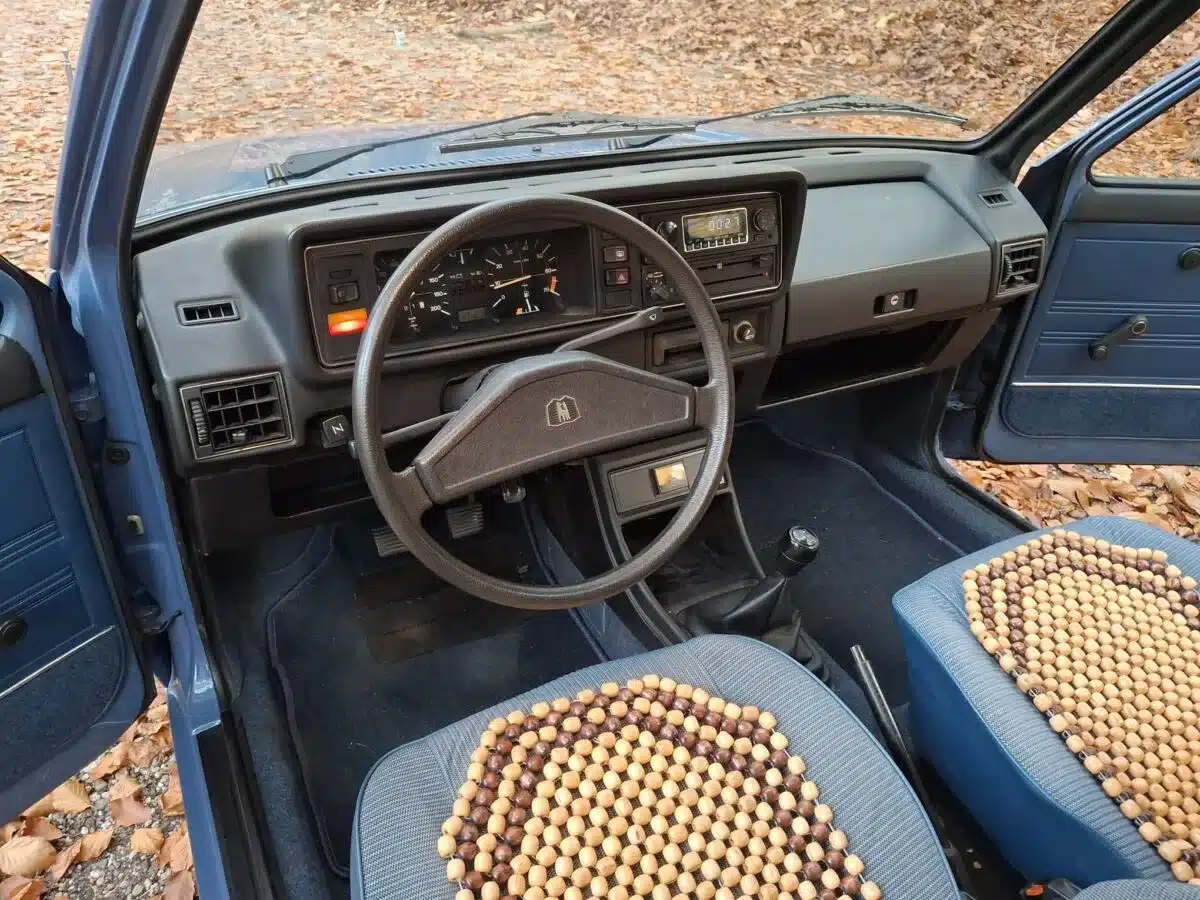 Innenraum eines Volkswagen Golf I von 1981 mit Blick auf das Lenkrad, Armaturenbrett und die Vordersitze mit Holzperlenauflagen.
