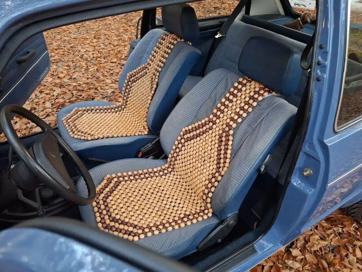 Innenraum eines Volkswagen Golf I von 1981 mit blauen Sitzen und typischen Holzperlen-Sitzauflagen, fotografiert im Herbstlaub