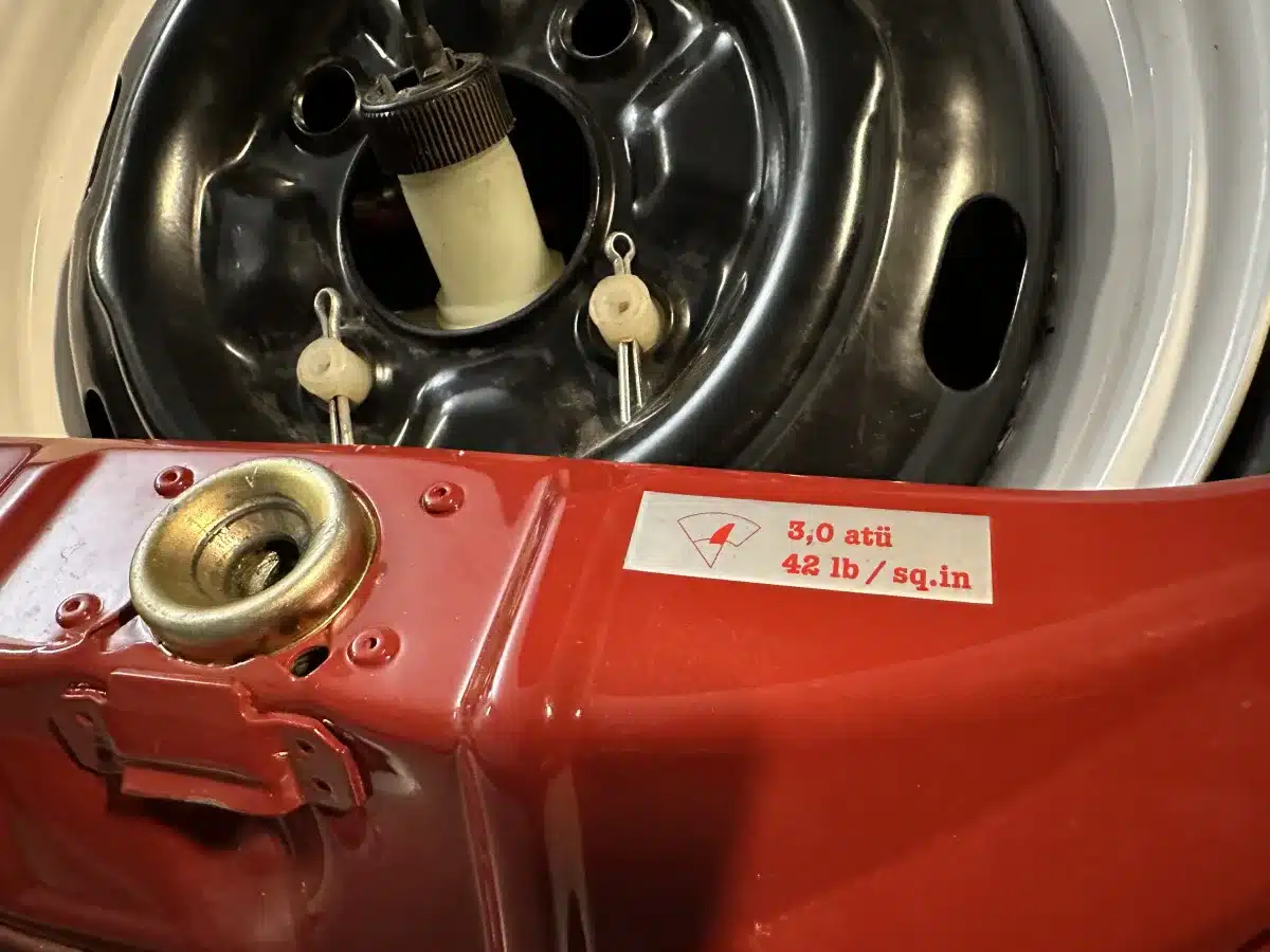 Nahaufnahme des Reserverads und eines Warnaufklebers im rot lackierten Kofferraum eines VW Spaarkever 1969.