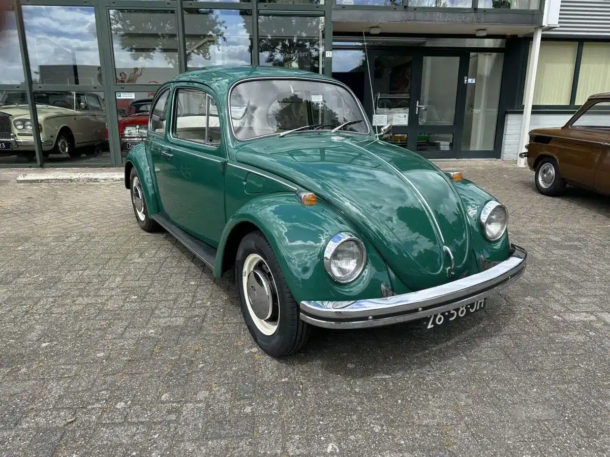 Grüner VW Käfer Spaarkever von 1969 auf einem Parkplatz vor einem Oldtimer-Autohaus.