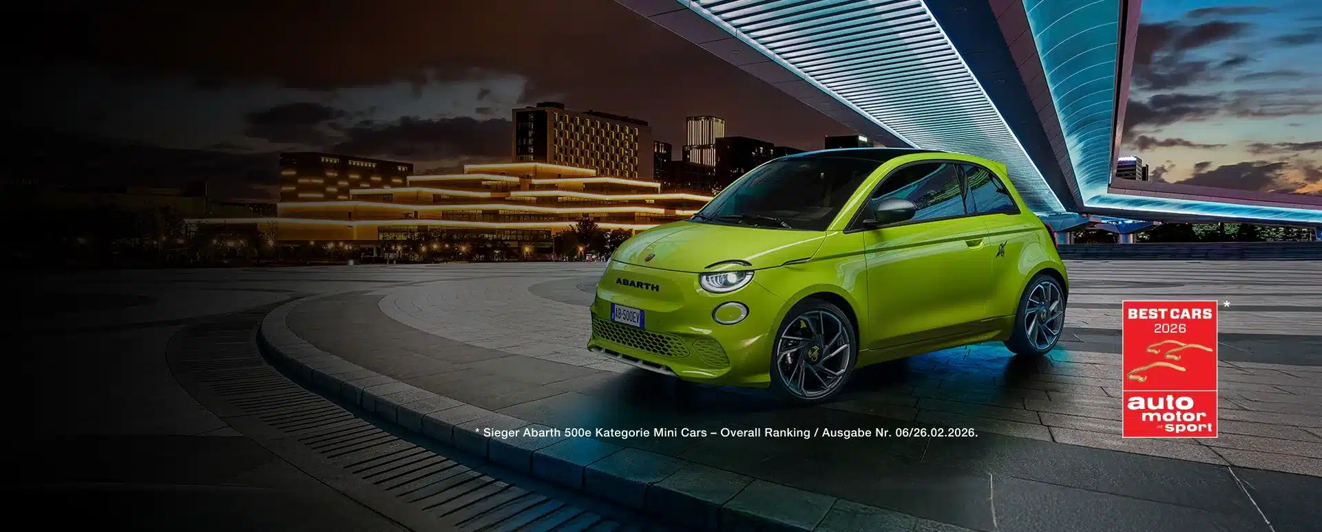 Abarth 500e in auffälligem Grün geparkt vor beleuchteten Gebäuden bei Nacht.